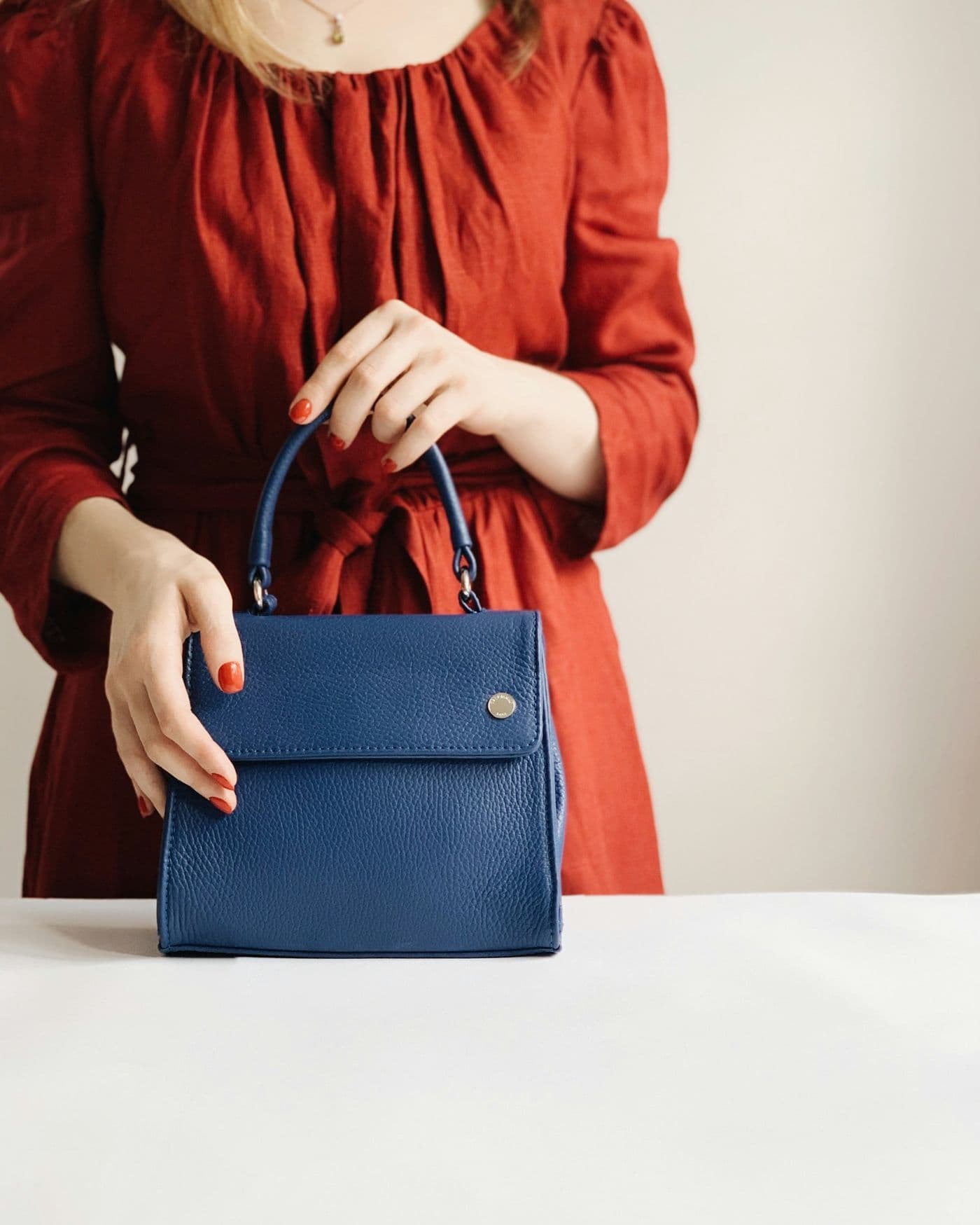 Hands holding a navy leather handbag against a red dress