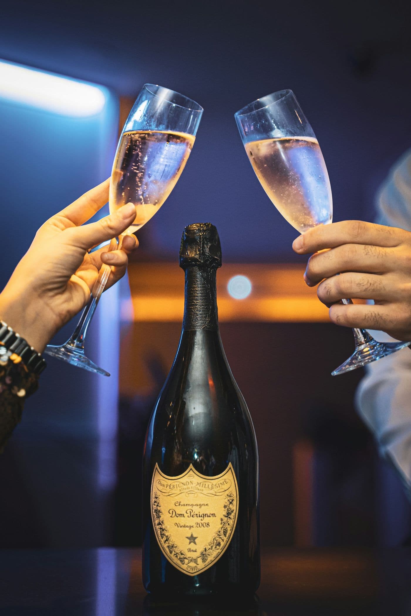Two champagne glasses raised over a bottle
