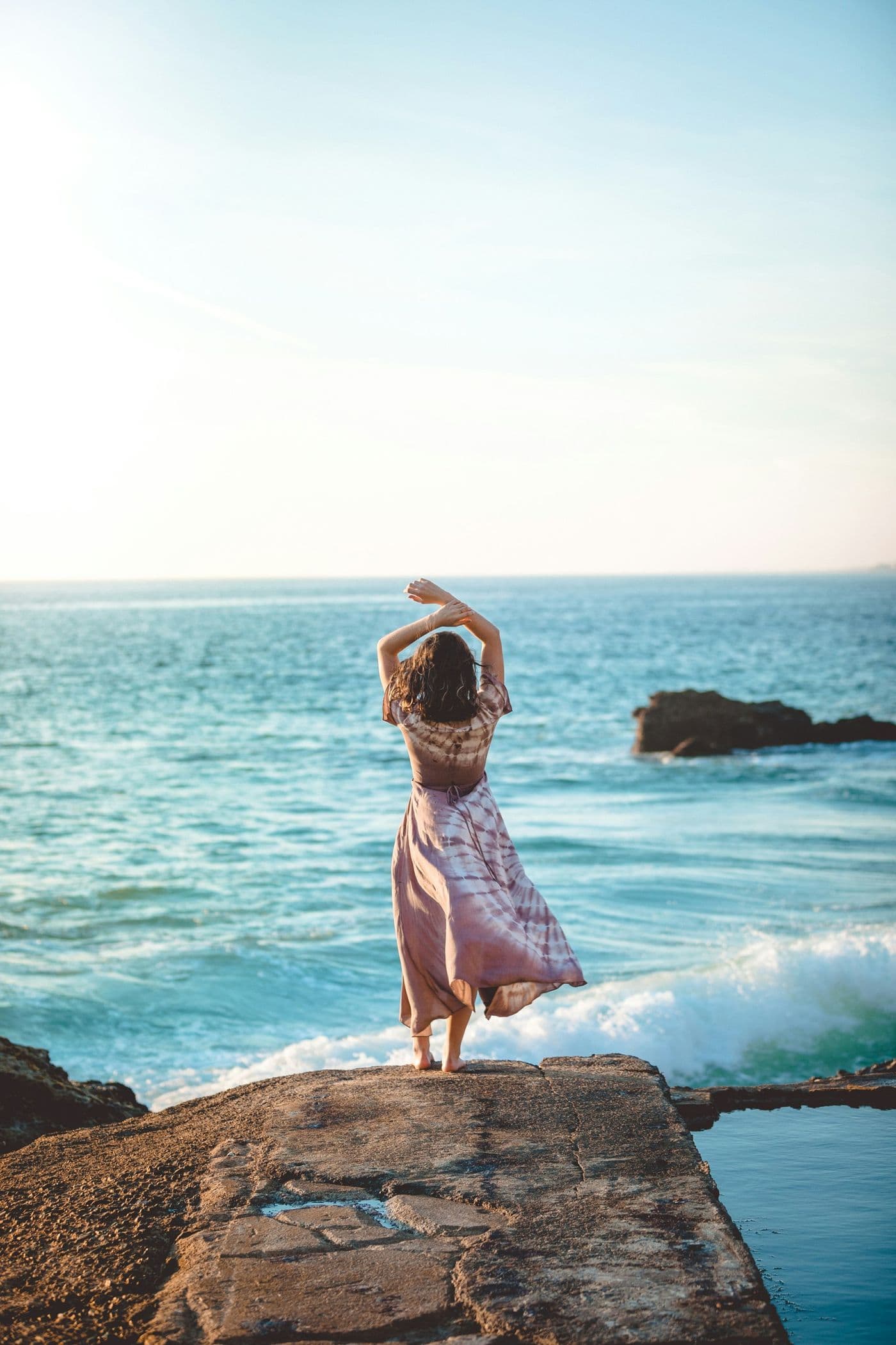 A woman in a summer dress on a seaside rock, seen from behind